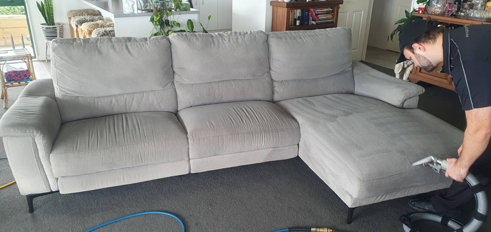 Technician cleaning a grey sectional sofa with an upholstery tool